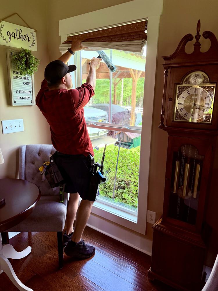 Ryan cleaning the top of a living-room window from the inside